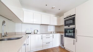 Una cocina moderna con armarios blancos, un lavamanos de acero inoxidable, un horno empotrado y un microondas.