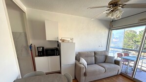 Ett kompakt bostadsutrymme med ett litet kök, en soffa, ett matbord och en balkong med utsikt.