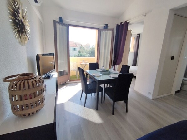 A dining area with a table, chairs, and a television. - Apartment with AC and parking, 4 guests, St-Pierre-La-Mer (Narbonne)