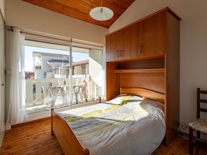 Ein Schlafzimmer mit einem hölzernen Bett, einem Einbauschrank und einer Glastür zum Balkon.