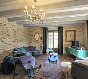 A stone-walled room with a chandelier, a sofa, a television, and a table. - Spacious house, parking - 6 guests (Les Eyzies)