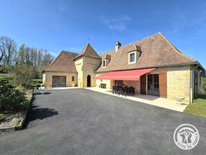 A stone building with a red awning, outdoor seating, and a clear sky. - Spacious house, parking - 6 guests (Les Eyzies)