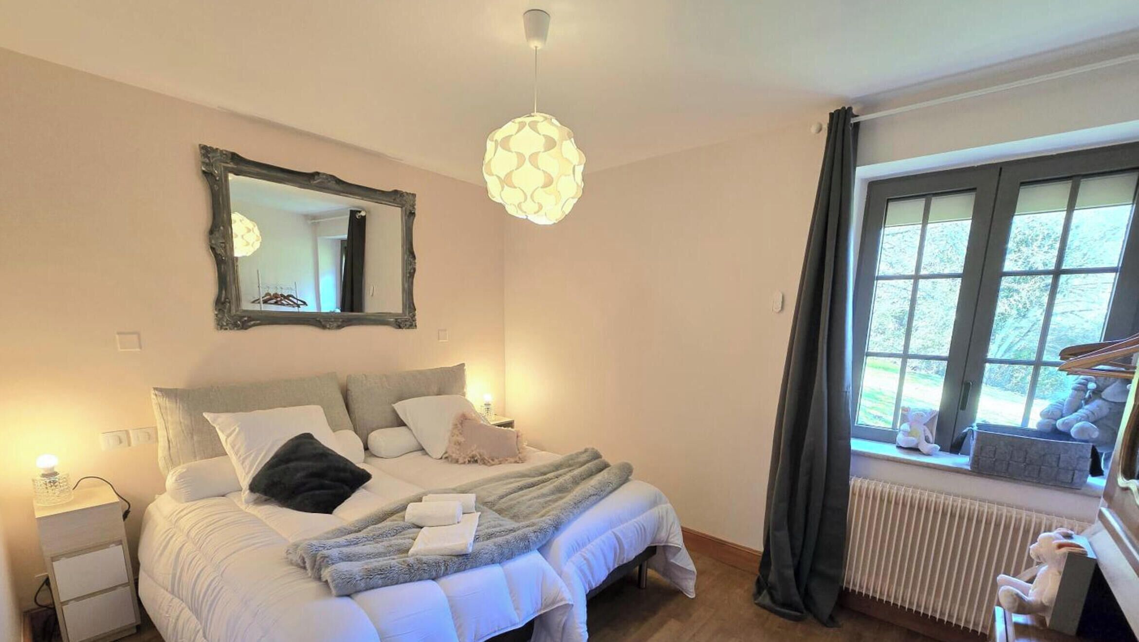 Un dormitorio con cama, mesita de noche, espejo, ventana y lámpara colgante.