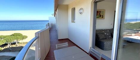 A balcony with a table and chairs, a sliding glass door, and a view of the ocean.