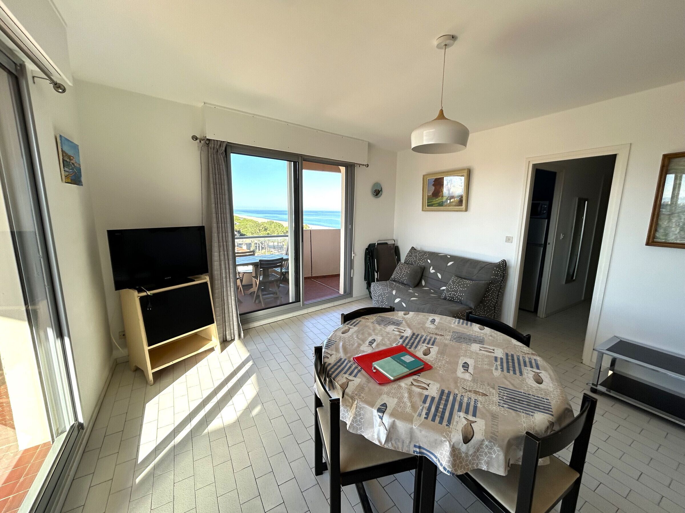 Une pièce avec une télévision, une table recouverte d’une nappe, un canapé et un balcon avec vue.