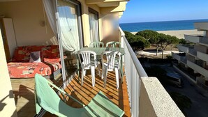 Un balcone con vista sul mare, un tavolo con sedie e un divano con cuscini decorati.
