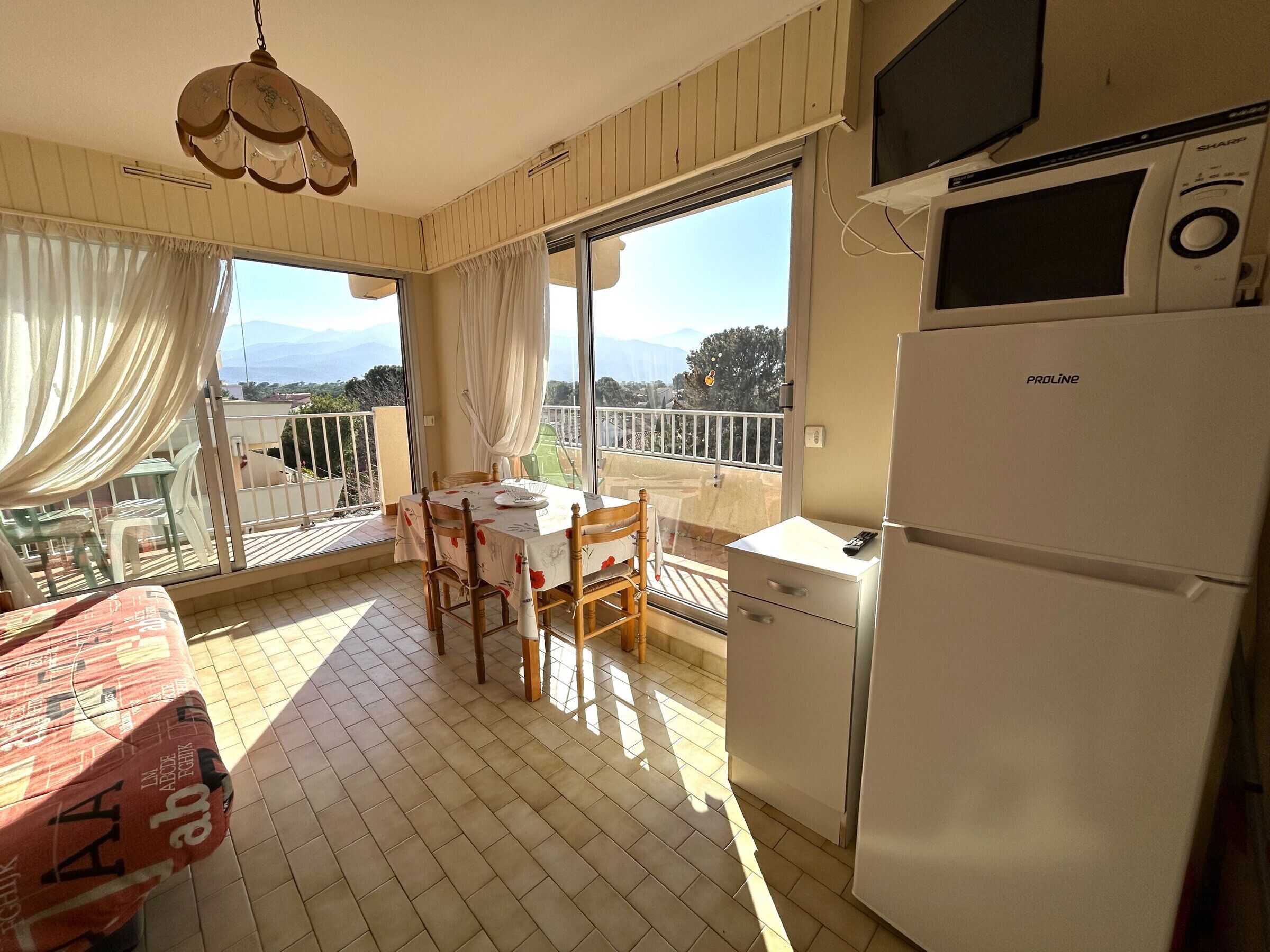 Uma varanda com mesa e cadeiras, uma geladeira e vista para o exterior.