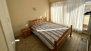 Una camera da letto con un letto in legno, un comodino con una lampada, una luce a parete e una finestra con tende leggere.