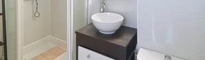 Et badeværelse med en hvid vask på en mørk bordplade, et bruseområde og et toilet.