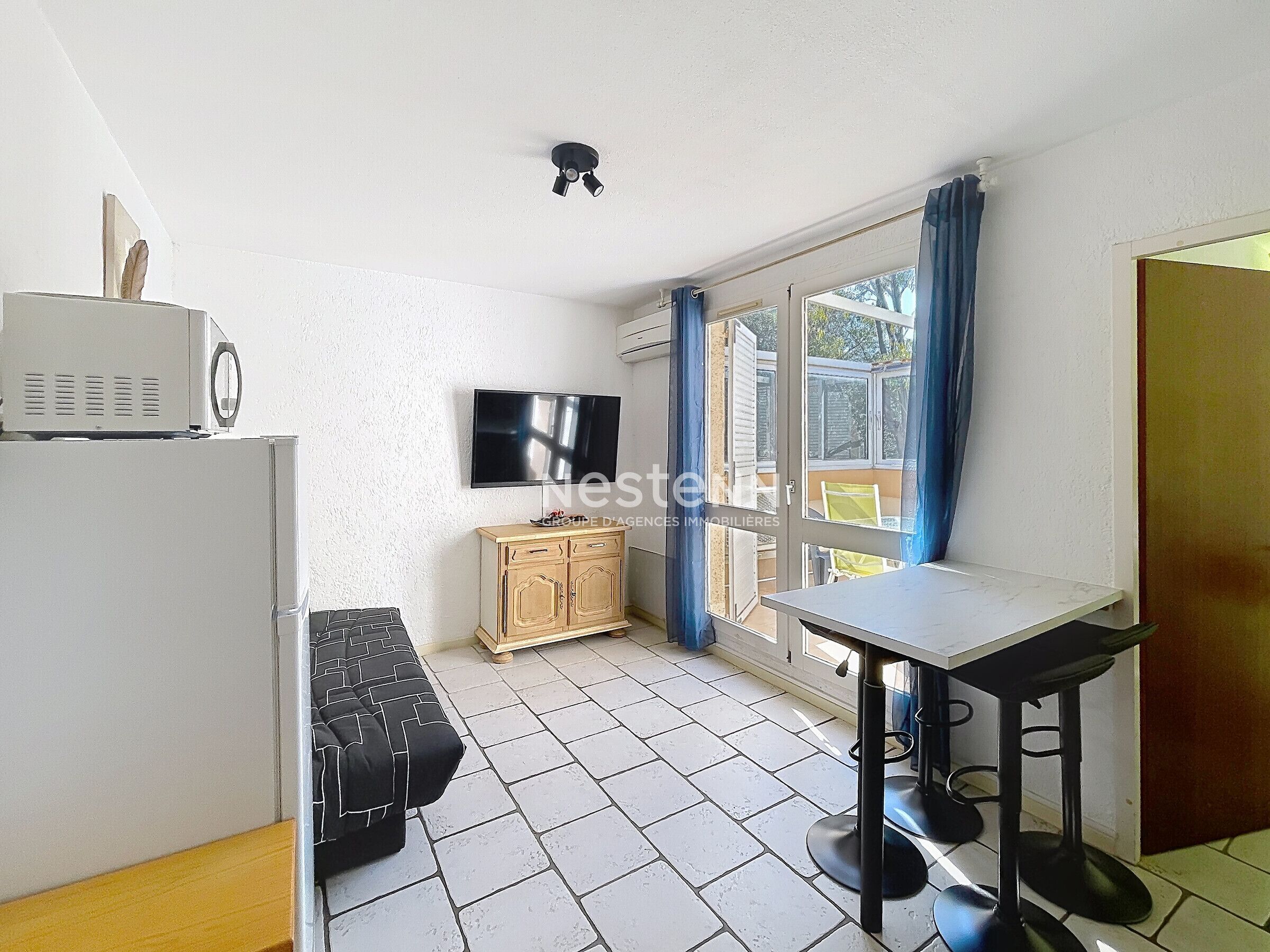 A compact kitchen with a refrigerator, a television, a wooden cabinet, and a dining area with a table and chairs.