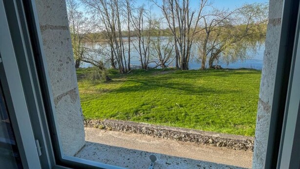 Näkymä ikkunasta, jossa avautuu näkymä ruohikkoiselle alueelle, jossa on puita ja vesistö.