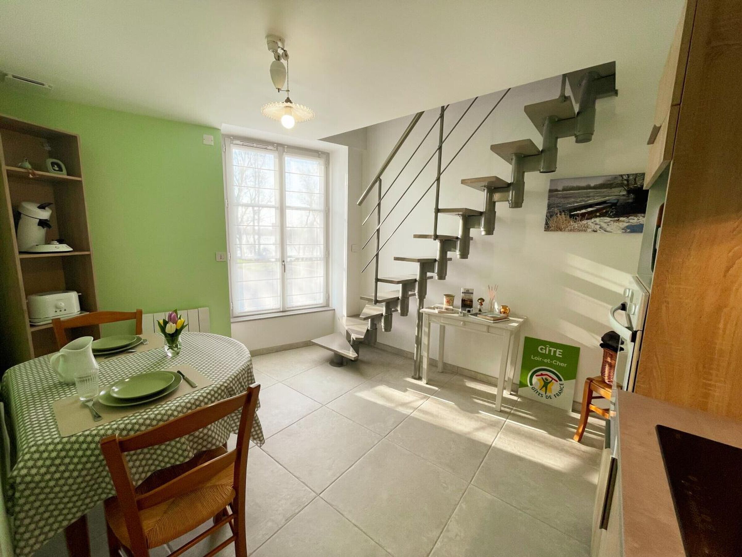A dining area with a table set for two, a staircase, and a view of the outdoors.