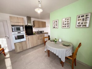 Une cuisine compacte dotée d’appareils électroménagers modernes, un coin repas avec une nappe à carreaux et un mur orné de photographies encadrées.