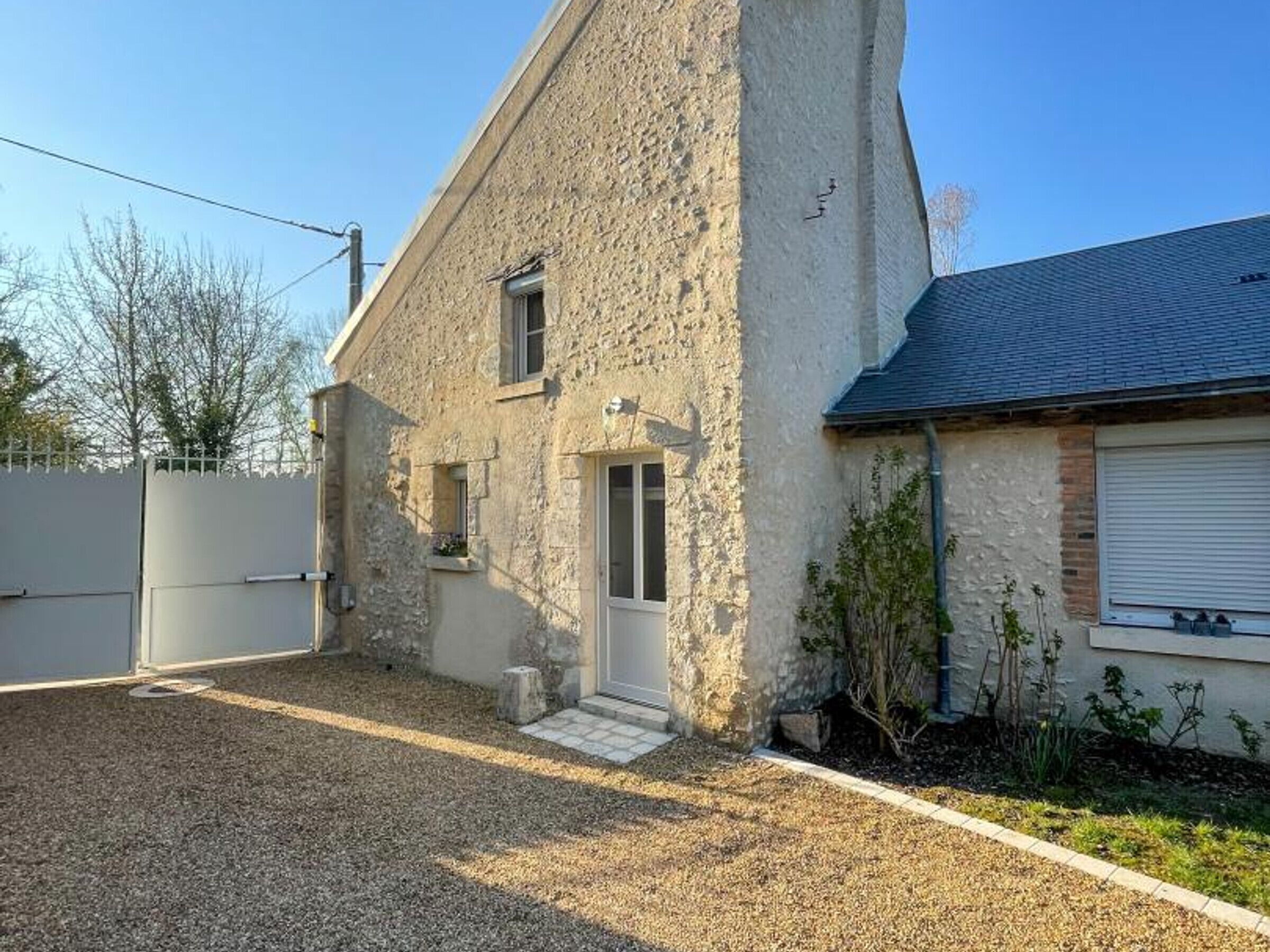 A two-story stone house with a gravel driveway and a gated entrance.