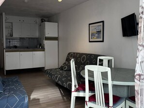 Ein kompakter Wohnbereich mit Küchenzeile, einer Couch, einem Esstisch mit Stühlen und einem an der Wand befestigten Fernseher.