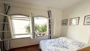 A bedroom with a bed, two windows, a view of greenery, and a tiled floor. - House in Port Grimaud with WiFi and private mooring, near the beach (Port Grimaud)
