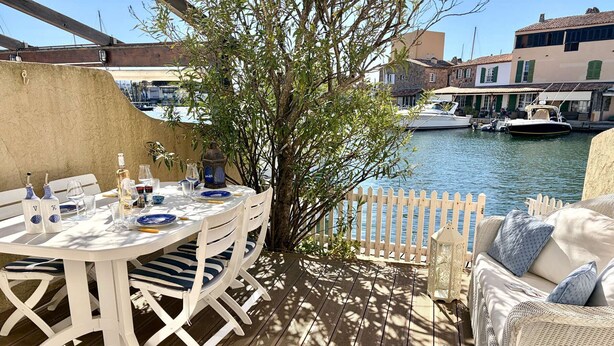 A wooden deck with a table set for dining, a wicker sofa, and a view of boats on water. - House in Port Grimaud with WiFi and private mooring, near the beach (Port Grimaud)