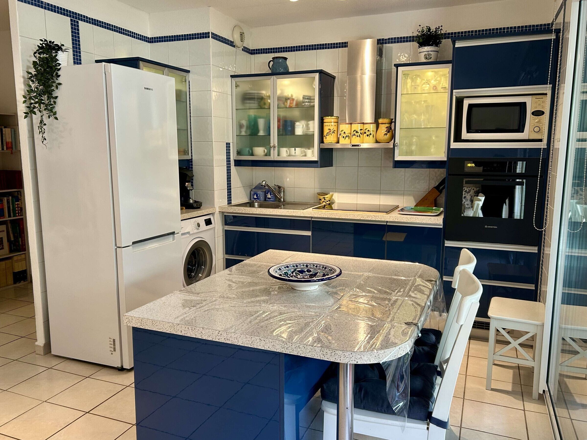 A compact kitchen with a refrigerator, washing machine, microwave, and a small dining area with a table and chairs.
