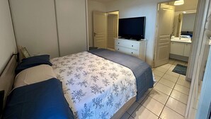 Una camera da letto con un letto, una televisione su una cassettiera, un bagno con lavandino e specchio, e una porta che dà su un'altra stanza.