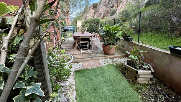 Una terrazza con tavolo e sedie, circondata da piante in vaso e una piccola area verde.
