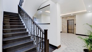 A modern hotel lobby with a marble floor, a staircase with black railings, and a potted plant. - Super Deluxe Room Hotel EL Portrait (Dehradun)