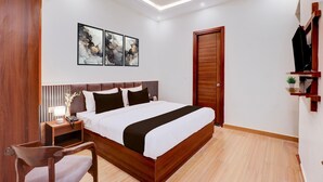 A modern hotel room with a large bed, a wooden headboard, a desk with a lamp, and artwork on the wall. - Super Deluxe Room Hotel EL Portrait (Dehradun)