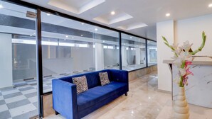 A modern lobby with a blue sofa, a vase of flowers, and a glass wall. - Super Deluxe Room Hotel EL Portrait (Dehradun)