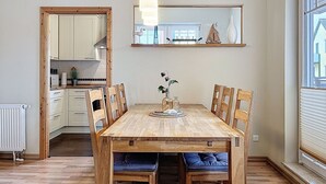 Ein Essbereich mit Holztisch, Stühlen, einer Pendelleuchte und Blick ins Freie durch ein Fenster.