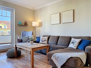 A living room with a sofa, a coffee table, a lamp, and a view through a window. - Beautiful apartment for 6 people with WIFI, TV and balcony (Wolgast)