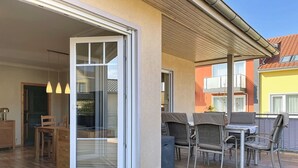 Eine offene Schiebetür führt auf eine Terrasse mit Gartenmöbeln und Blick auf benachbarte Gebäude.
