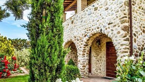 A stone building with arched doorways, surrounded by lush greenery and flowering plants.