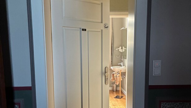An interior hallway with a white door marked with the number 5, leading to a bathroom with a sink and mirror. - Guesthouse LeLo (5) (Solingen)