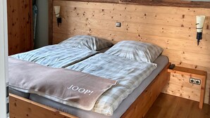 A wooden bed with a headboard, a bedside table with a lamp, and a towel with text. - Guesthouse LeLo (5) (Solingen)