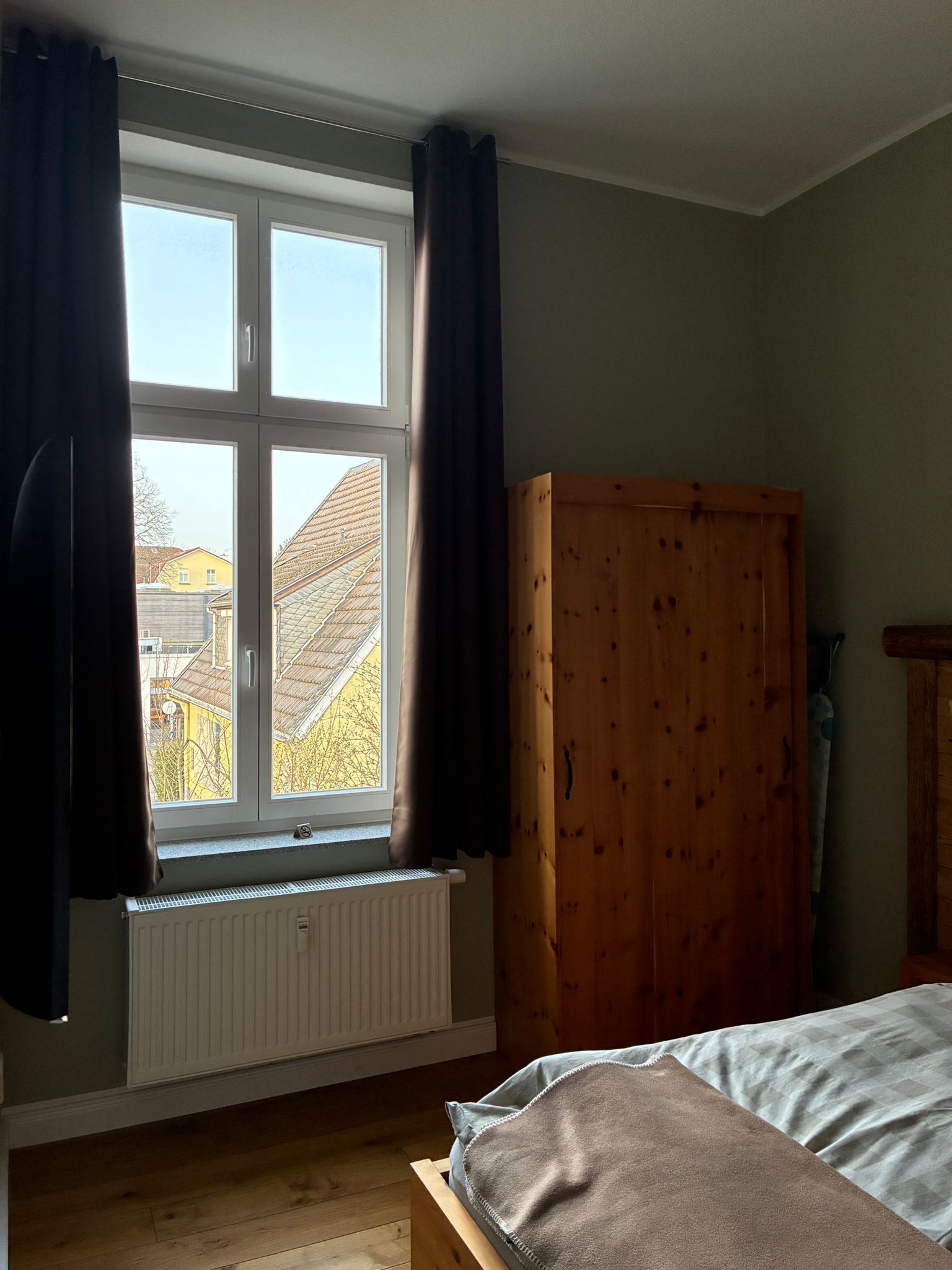 Un dormitorio con ventana, radiador, armario de madera y cama.