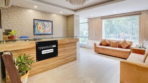 A reception area with a wooden desk, a sign reading 'Townhouse Oak,' a large window, and a sofa. - Townhouse Oak Ongc Crossway (Dehradun)
