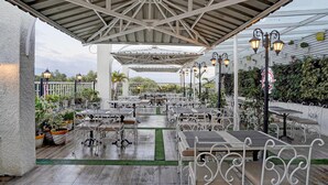 An outdoor patio with tables and chairs, a covered seating area, and decorative lighting. - Townhouse Oak Ongc Crossway (Dehradun)