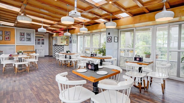 A spacious dining area with wooden ceiling beams, white chairs, and tables. - Townhouse Oak Ongc Crossway (Dehradun)