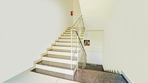 A staircase with white steps and metal railings, leading to a landing with a fire extinguisher mounted on the wall. - Deluxe Kalamassery Near Medical College (Kanayannur)