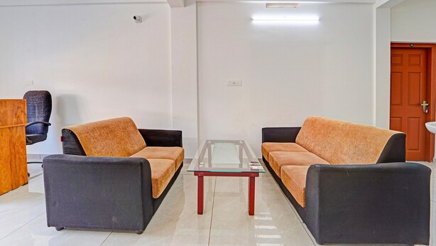 A room with two sofas, a glass-top table, a wooden side table, and a door. - Deluxe Kalamassery Near Medical College (Kanayannur)
