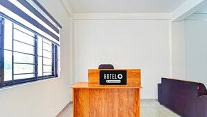 A hotel reception desk with a sign, a window with blinds, and a sofa. - Deluxe Kalamassery Near Medical College (Kanayannur)