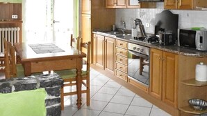Une cuisine avec des meubles de rangement en bois, une table à manger, des chaises, une cuisinière et un four à micro-ondes.