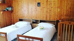 Une pièce avec deux lits en bois, un berceau, un luminaire suspendu et un sol carrelé.