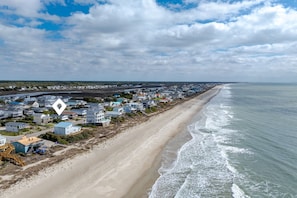 A coastal residential area with houses along the beach, a clear sky, and a calm sea. - Ocean Views + Steps to the Beach + 3BDR + King Bed (Oak Island)