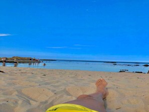Cena de praia com céu claro, areal arenoso e águas calmas.