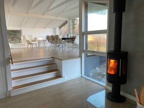 A modern interior with a wood-burning stove, a dining area with chairs, and a staircase. - 4 Star Holiday Home in Allinge (Allinge)