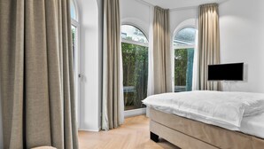 A bedroom with a bed, a TV, and large windows with curtains. - Experience Luxury at Ocean's Retreat in Westerland, Sylt (Sylt)