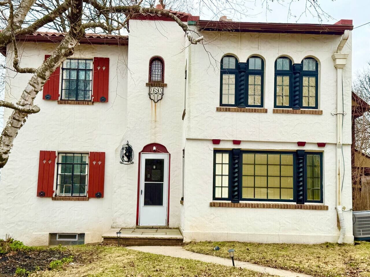 Charming two-story stucco home with red shutters, arched windows, and a centered entry. A large front window adds natural light, while a tree and small yard enhance its inviting curb appeal. Close to SU, hospitals and downtown.