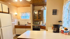 Una cocina con refrigerador, microondas, cafetera y ventana con cortinas de encaje.