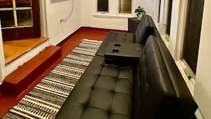 Una sala de estar con un sofá negro, una televisión y una escalera que lleva a un balcón.