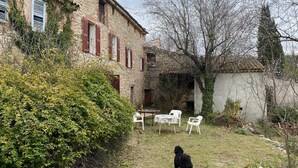 Ein Gebäude aus Stein mit Fensterläden, einem Rasen und einem Hund.